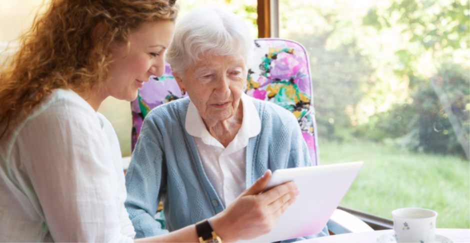 A woman holds up a tablet computer to show an elderly woman.