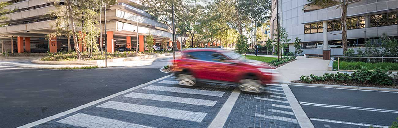 Red car driving through quiet campus intersection.