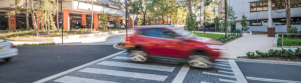 Red car driving through quiet campus intersection.
