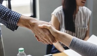 Two people shaking hands with a woman in the background