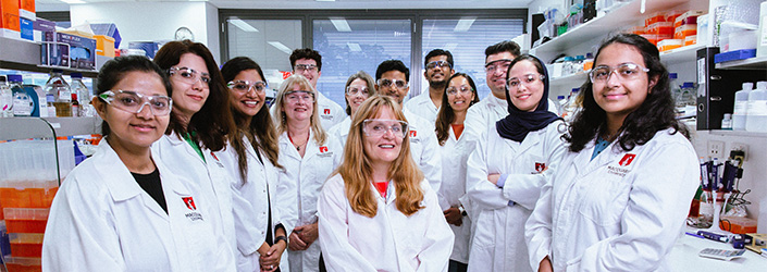 The 13-person cellular biology team in lab coats smiling at the camera.