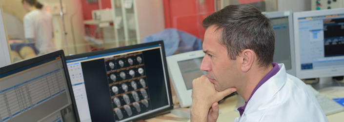 A medical professional sitting at a desk looking at computer screens containing x-rays and test results.