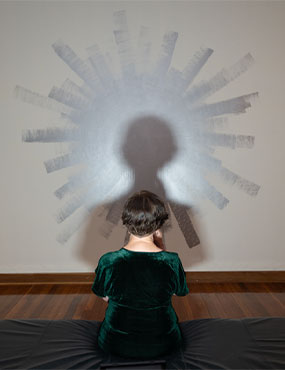 Person sitting on gallery bench with their shadow projected to artwork in front of them