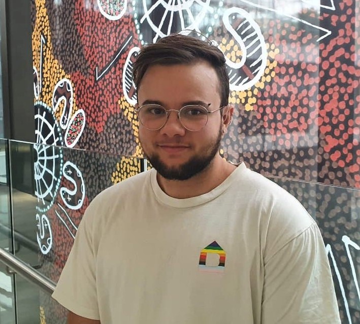 Photo of Zac Roberts standing in front of artwork by Aboriginal artist Dylan Barnes