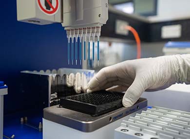 A medically-gloved hand holding a plastic board, with medical samples attached to a machine.