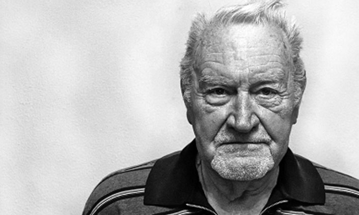 A black and white image of an elderly man looking stoically at the camera.