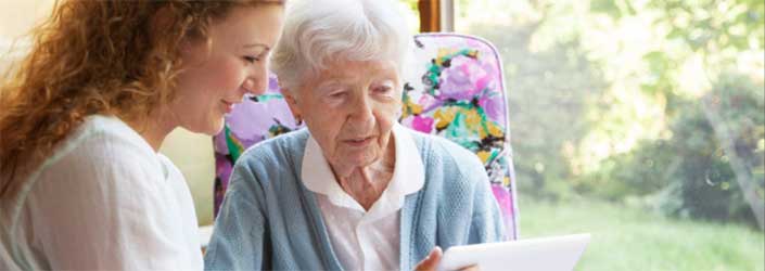 A young healthcare worker show an elderly woman something on her laptop