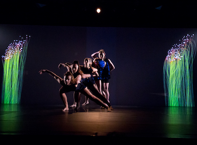 Six student dancers performing at Macquarie University’s 50th Anniversary Gala. They are posing in a line, one behind the other with those at the front crouching and those at the back standing, between two close-up images of glowing plant life or green fibre optic cables.