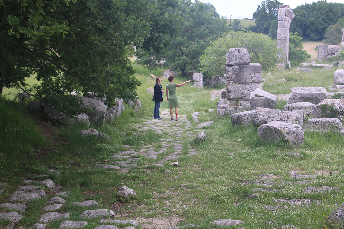 Two women standing amongst ancient stone ruins overgrown with grass and trees