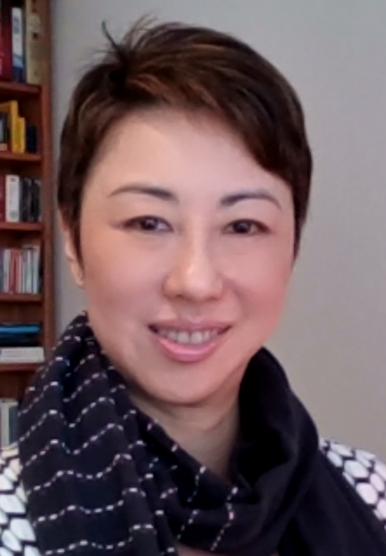 Smiling woman with short, dark brown hair and brown eyes. She is wearing a navy blue scarf and a white and black striped shirt.