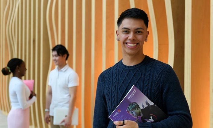 TJ Pham holding a book standing on campus