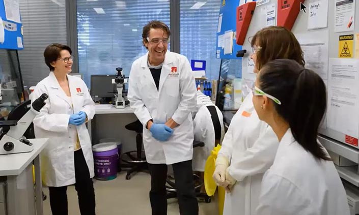 Group of people facing each other wearing lab coats standing in a lab