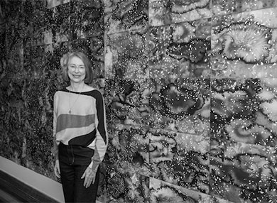 Black and white photo of Paula Daws in front of artwork on wall