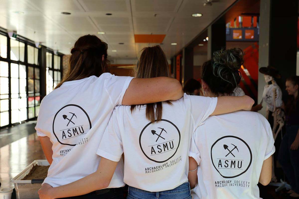 Three people wearing t-shirts with ASMU logo standing together with backs towards the camera and arms around each other