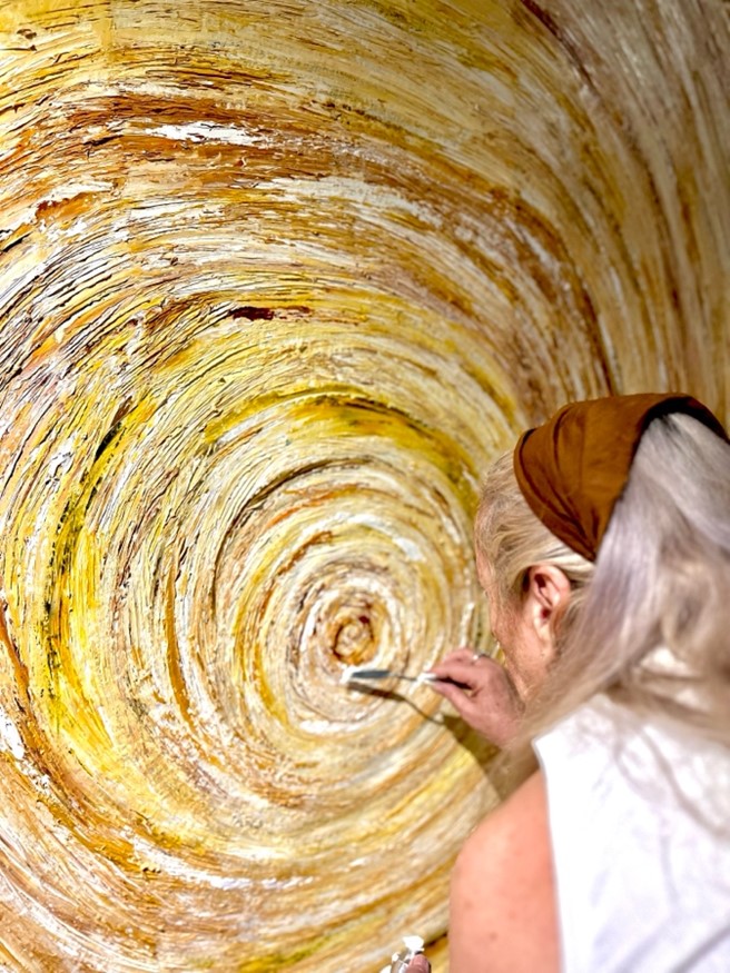 Liz Cameron painting an Indigenous Australian painting with yellow swirls 
