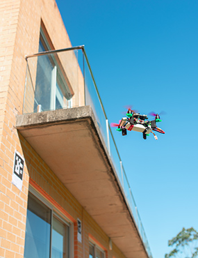 A drone hovering under a balcony near a marker stuck to a brick wall.