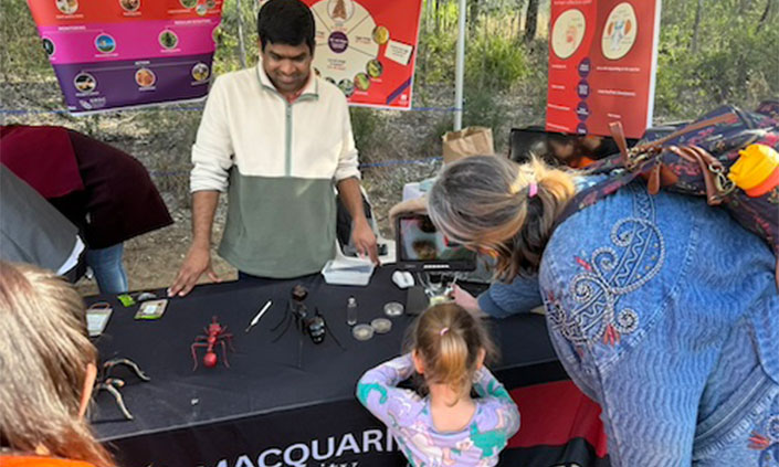 Child and carer looking at model bugs at a marquee, man standing behind desk smiling
