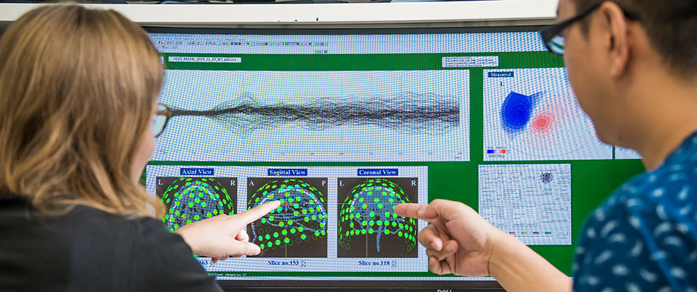 Two people looking and pointing at brain scan images on a computer screen