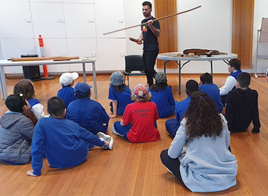 Children sitting on the floor listening to indigenous demonstration