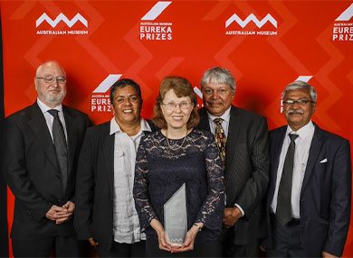NISEP representatives standing infront of orange backdrop with their 2019 Eureka Prize for STEM Inclusion.