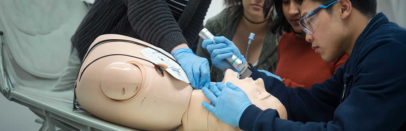 A person wearing gloves and using a medical instrument on a simulation mannequin.
