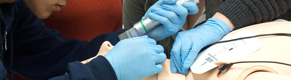A person wearing gloves and using a medical instrument on a simulation mannequin.