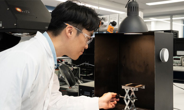 Man in lab coat testing solar cell inside box with light