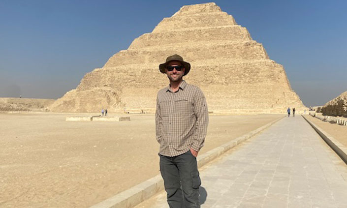 Professor Tim Ralph facing the camera in front of ancient pyramid.