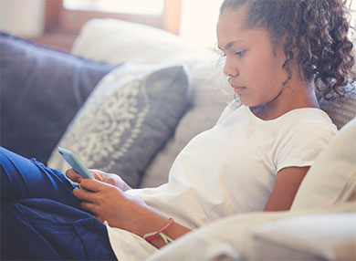 An Aboriginal girl sitting on a couch, looking at her phone.