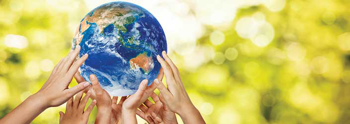 Hands holding up the Earth in front of a leafy background.