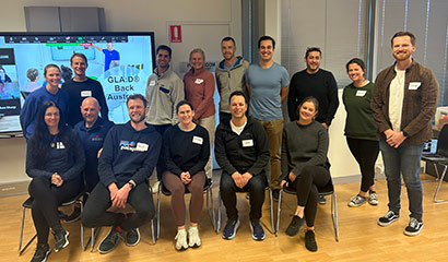 Mark Hancock, Stephen Sharp, Hazel Jenkins and other team members stand and sit smiling in front of a screen displaying GLAD Back Australia training materials.