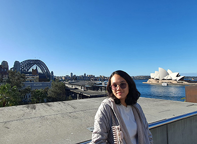 Student Nina Andrea Maranon is in a rooftop posing for a photo on a sunny day. The Opera House and the Harbour Bridge are in the background.