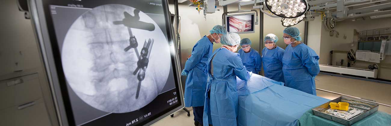 A group of people in an operating room dressed in scrubs, with grey screen showing the operation.
