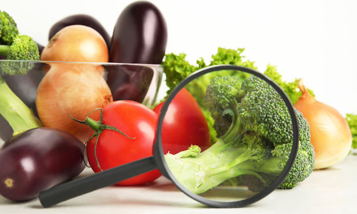 Variety of vegetables in a bowl with some loose. Magnifying glass on table magnifying a vegetable