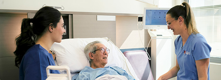 Two medical professionals with a patient in a hospital bed.